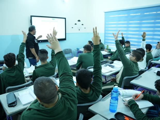 طلاب يرفعون أيديهم للمشاركة أمام السبورة الذكية