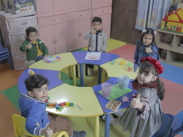 أطفال الروضة يلعبون بالمكعّبات على طاولات ملوّنة