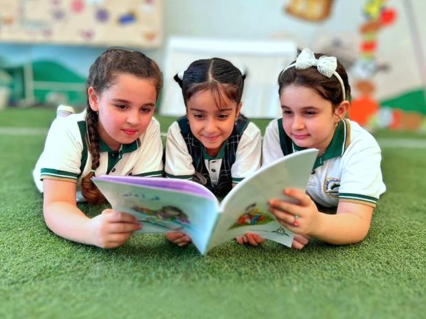 ثلاث طالبات يقرأن كتاباً على المساحة الخضراء